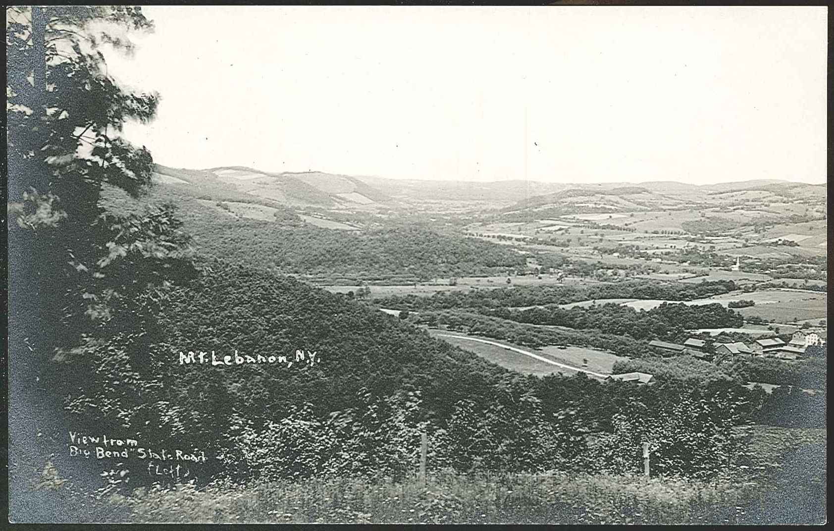 An old photo of a valley with trees and hills.